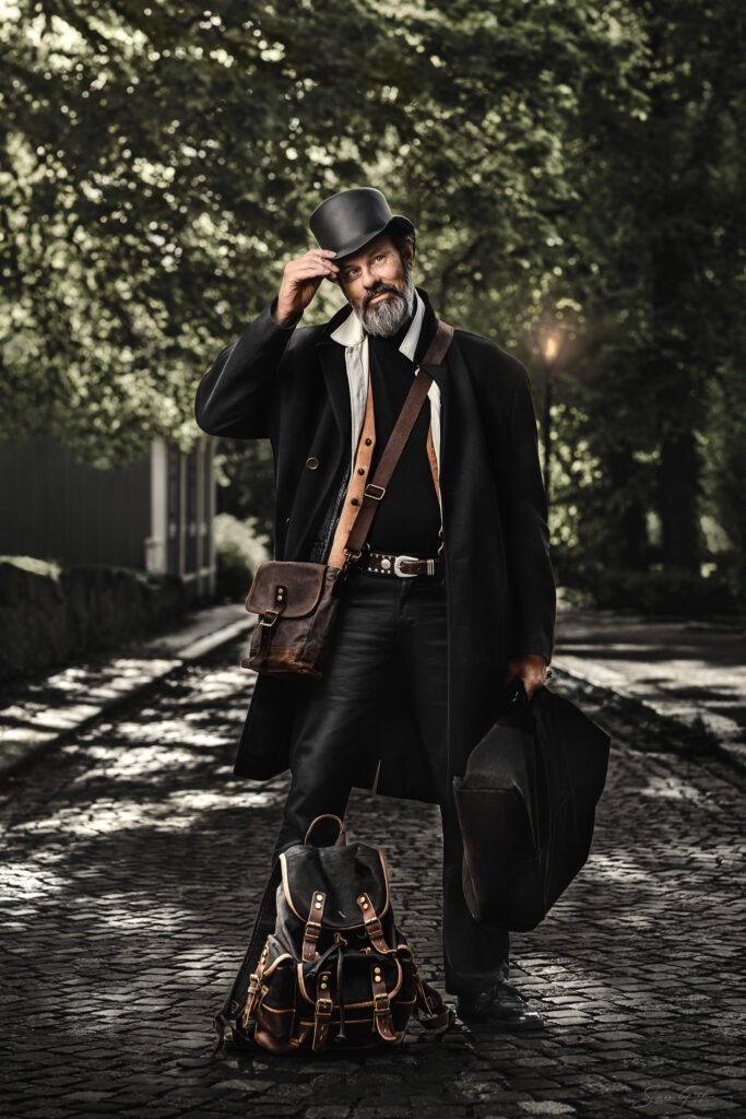 Fotoav en man i svart hatt och lång svart kappa. ståendes på en kullerstensbelagd gata