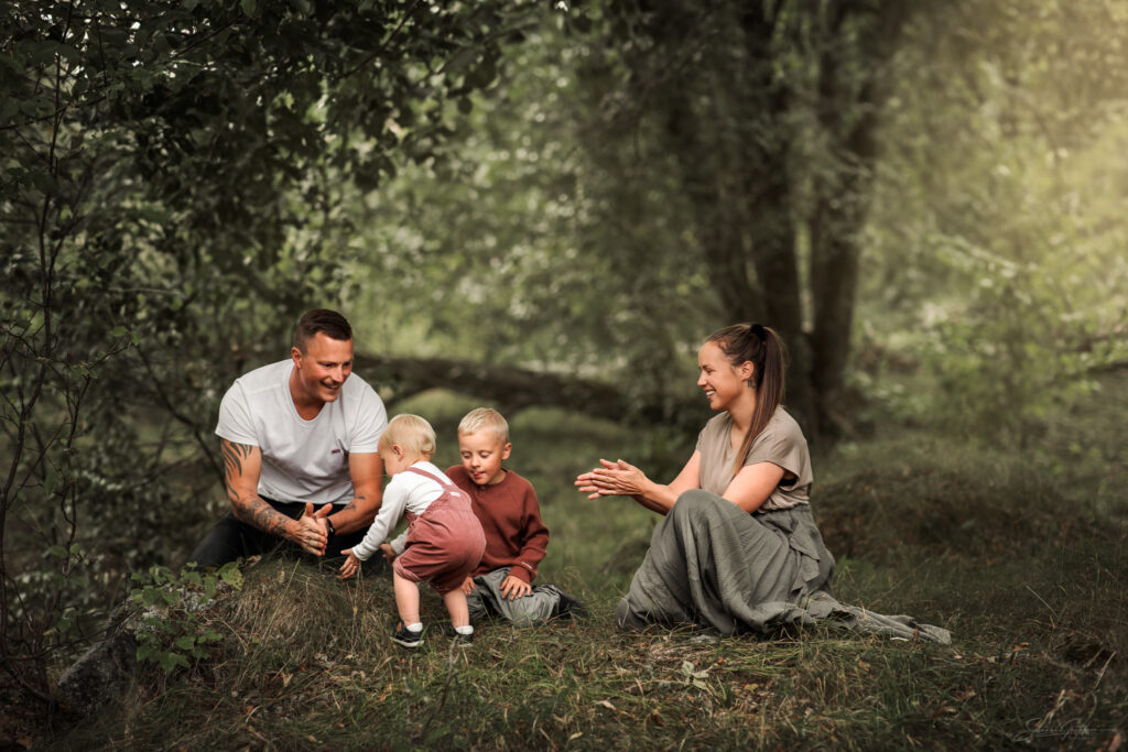 Familjefotografering utomhus i grönskande miljö.