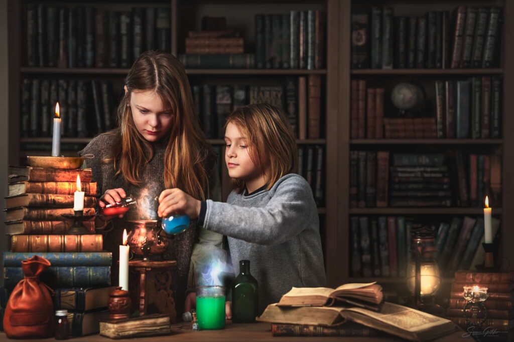 Barnfoto med fantasykänsla – syskon bland böcker och ljus gör experiment under barnfotografering